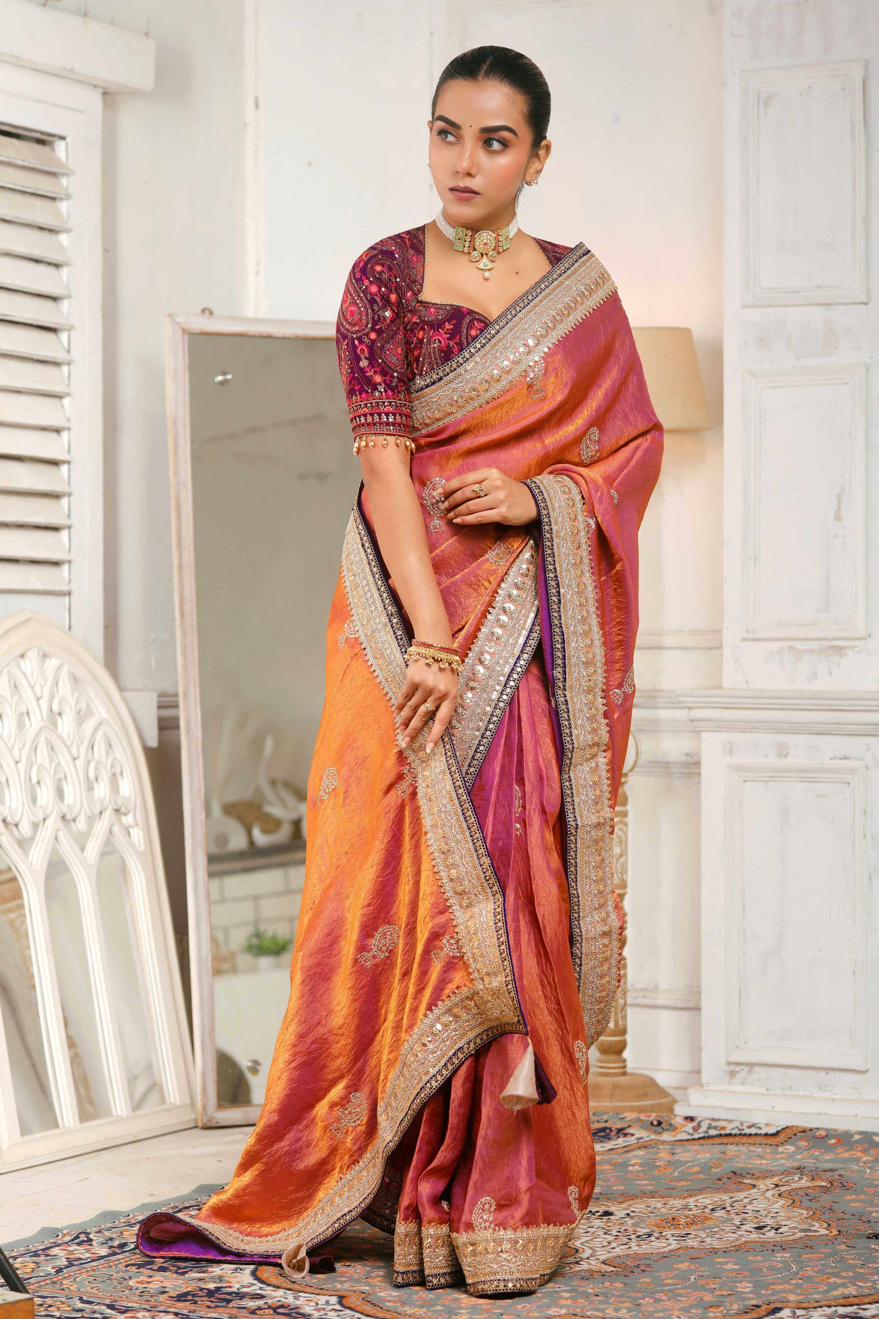 Model wearing a coral pink crushed tissue saree with embellished borders, showcasing elegant style and grace.