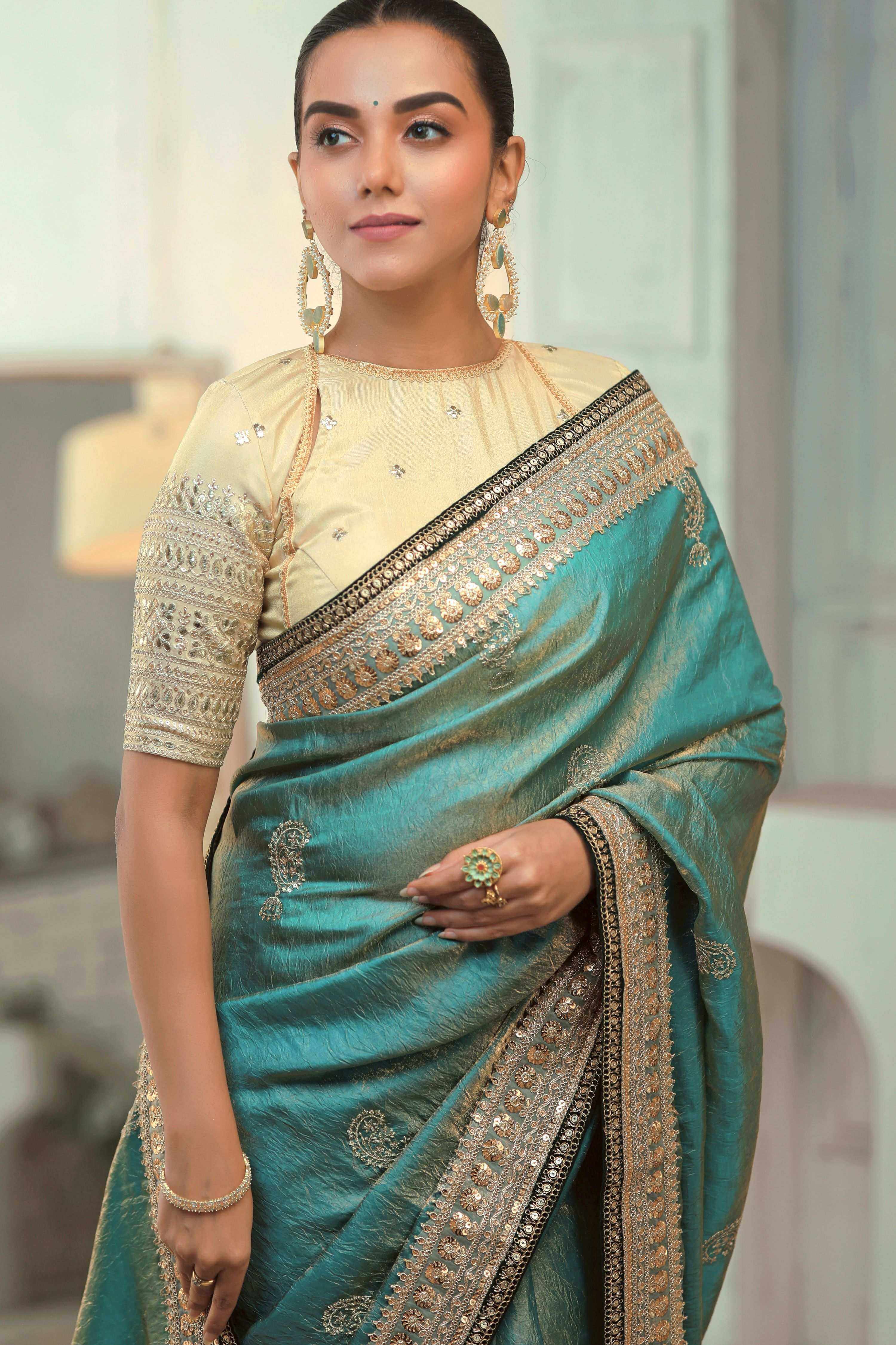 Teal blue saree with champagne blouse, featuring embroidery and intricate borders.