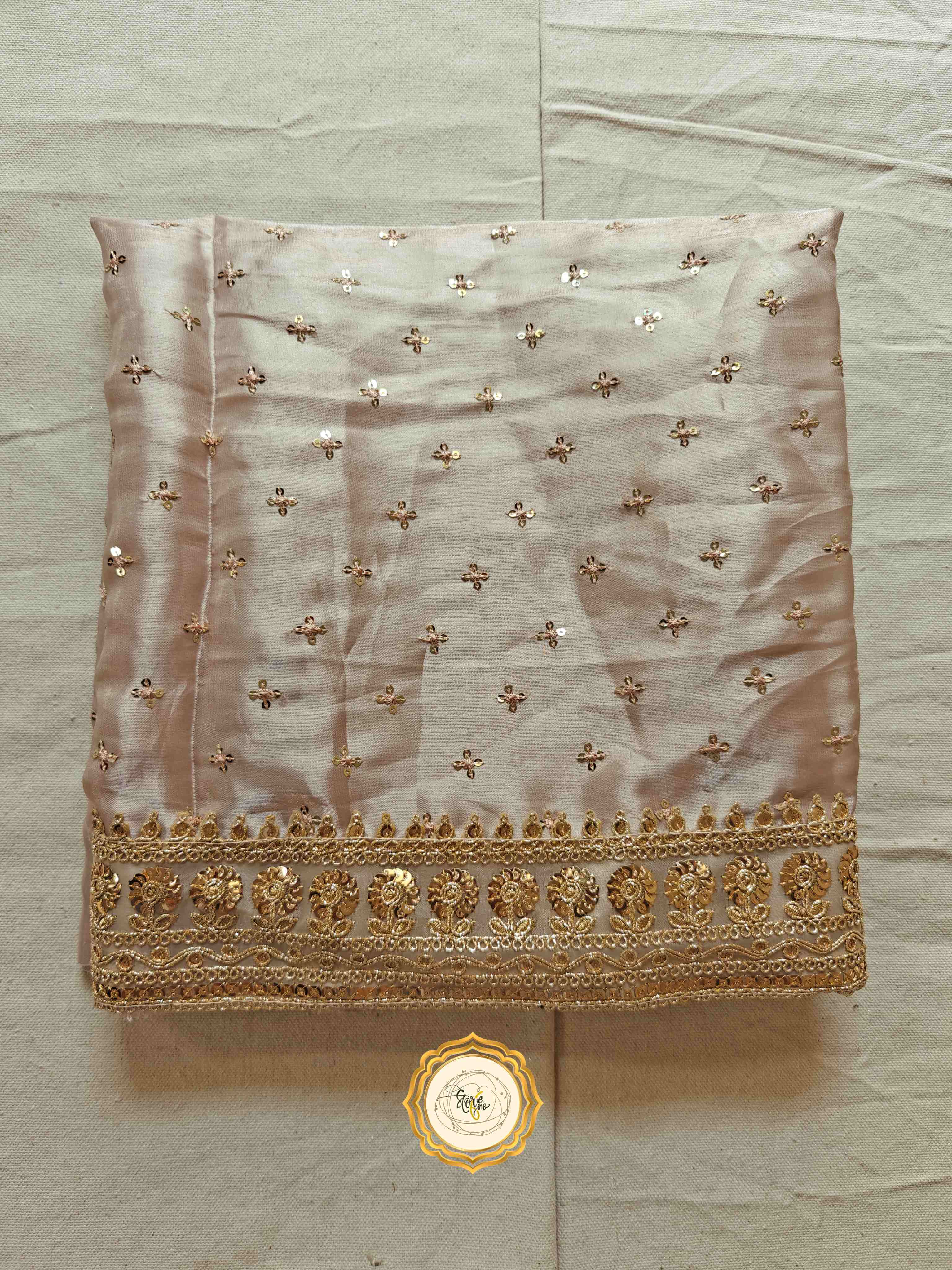 Elegant satin saree with blouse showcasing intricate golden embroidery and sequins on a sandstone organza fabric.