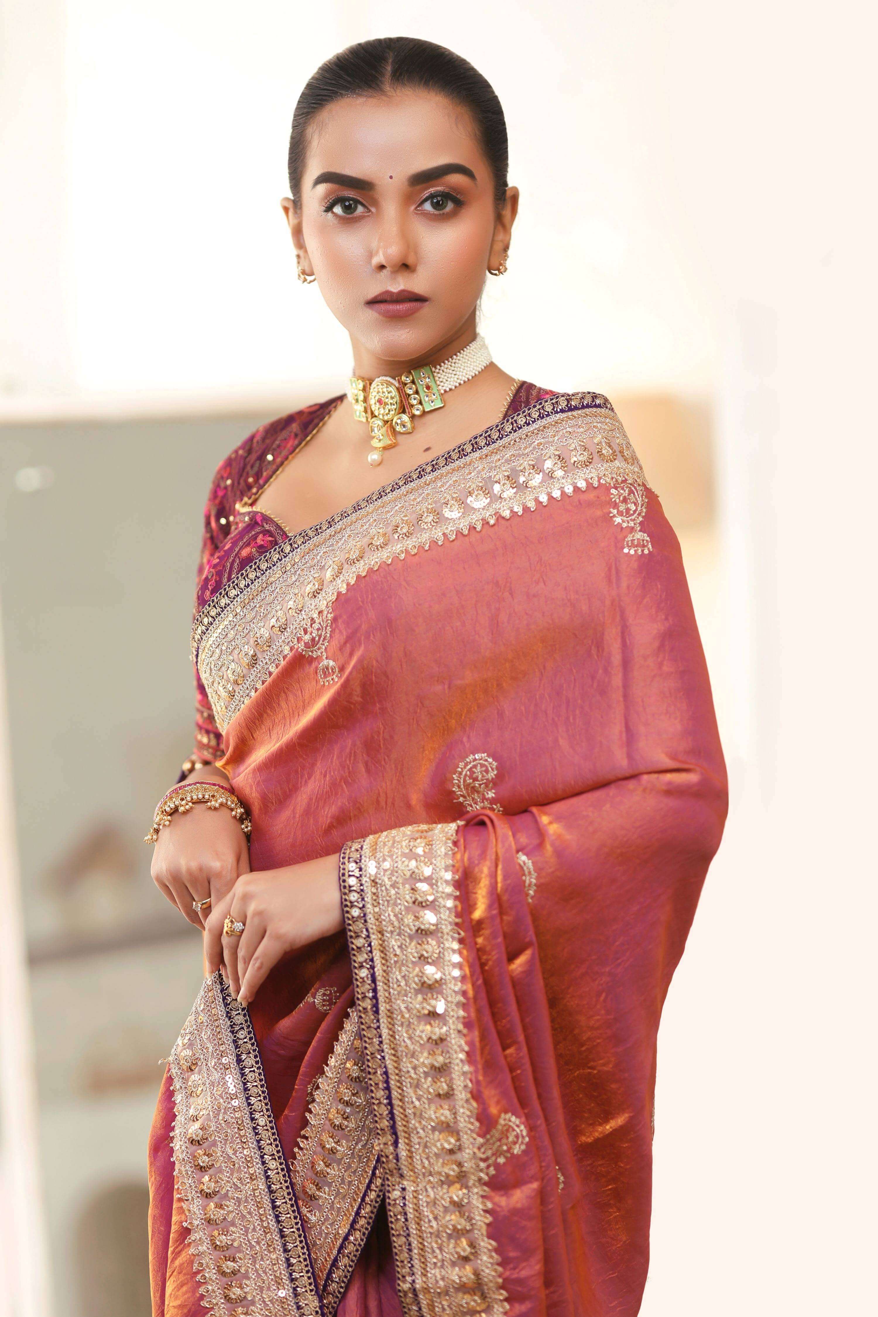 Model wearing a coral pink crushed saree with embellished borders and a wine georgette blouse.