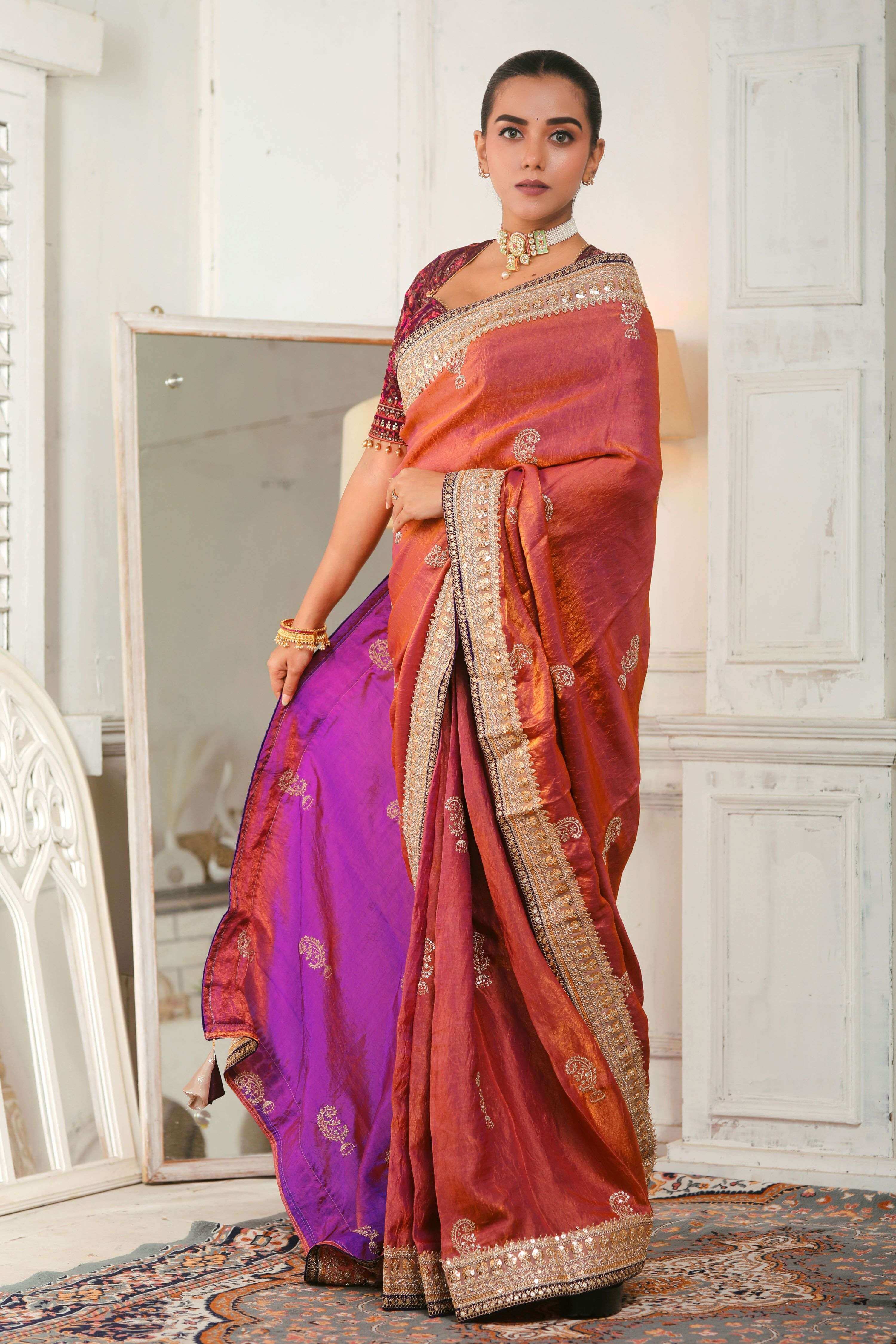 Model wearing a coral pink crushed tissue saree with embroidered borders, showcasing elegant traditional attire.