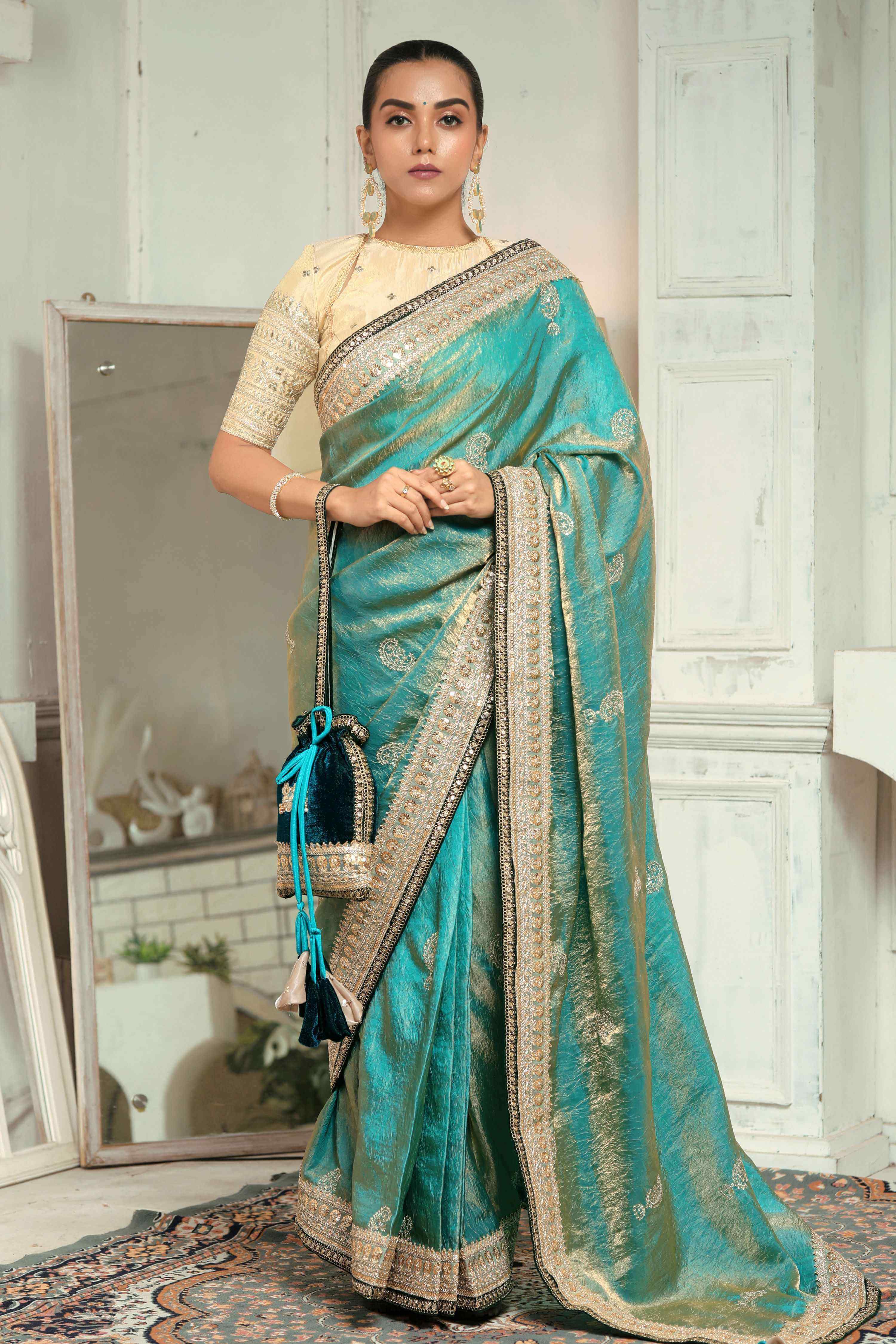 teal blue saree with champagne blouse elegantly worn, showcasing intricate embroidery and golden borders.