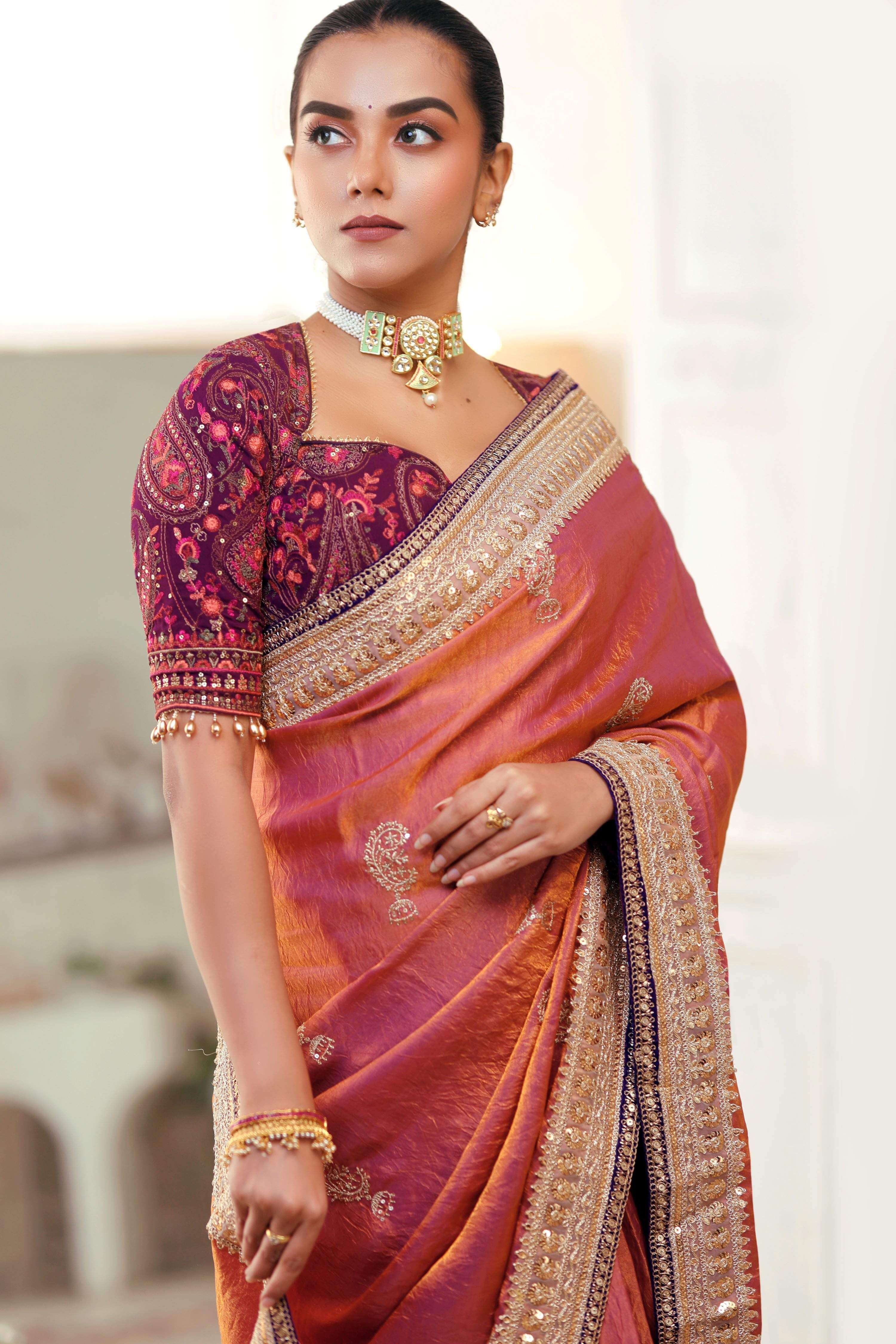Elegant model draped in a coral pink crushed saree, showcasing intricate embroidery and a stylish blouse.